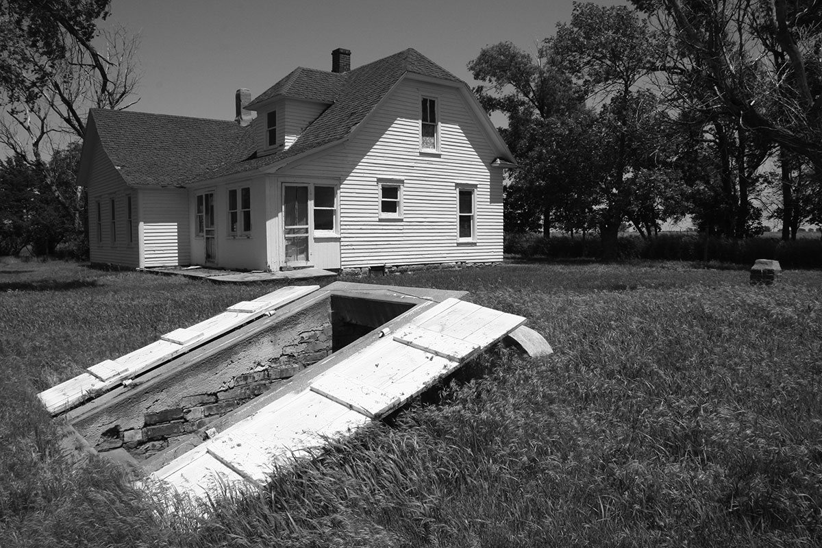 black and white photo of farmstead with root cellar in foreground and house in background