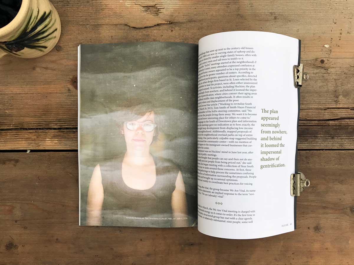 The New Territory inside page with a portrait of a woman behind a screen door, text, and a pull quote; the magazine is on a warm wood background next to a coffee mug.