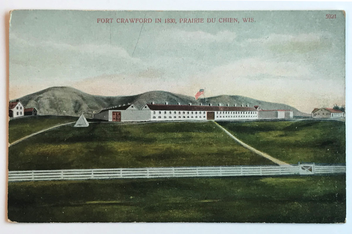 vintage postcard depicting white fort on green field. Red text on top over blue sky says, "Fort Crawford in 1830 Prairie du Chien, Wis."
