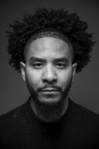 black-and-white portrait of Doug Barrett, a Black man with an afro and beard; Doug is looking into the camera with a placid expression