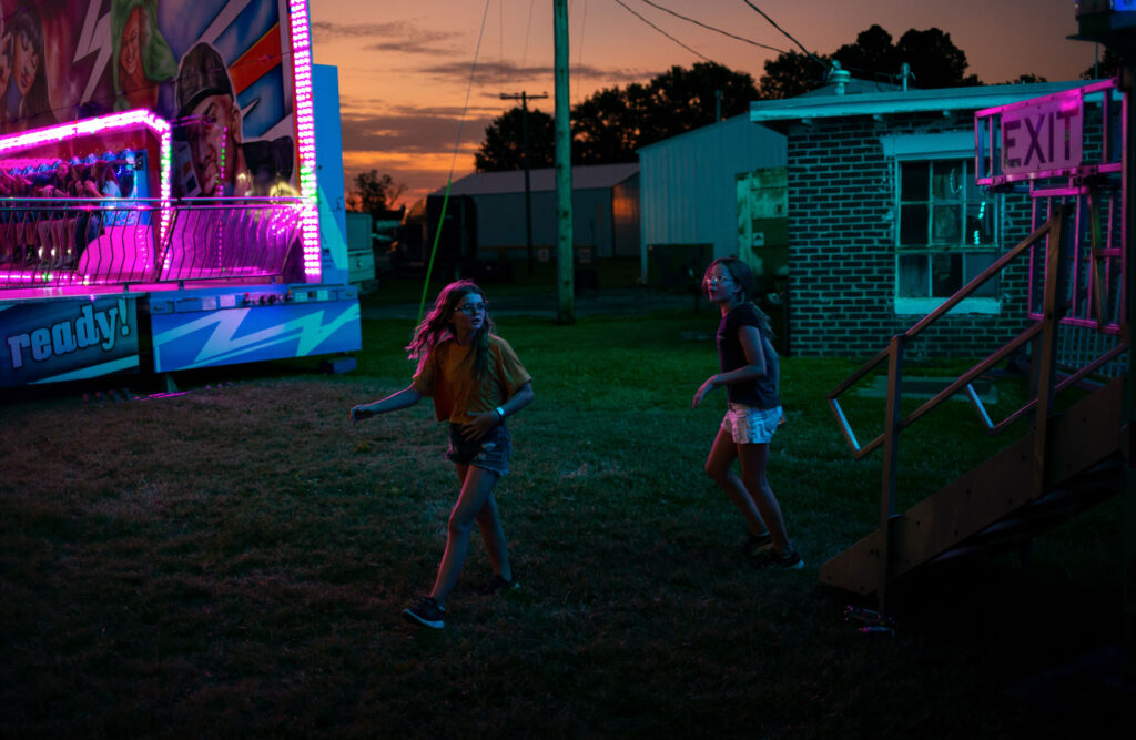 moody photograph of two tweens walking the edges of a fairground at sunset