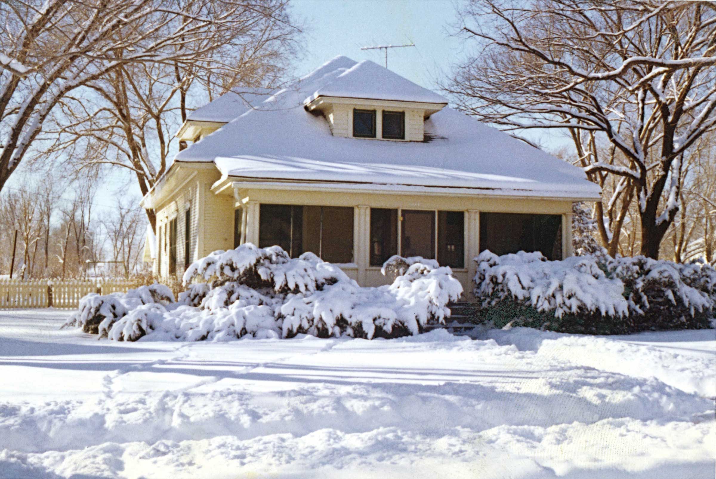 house with lawn, shrubs, and roof covered in snow