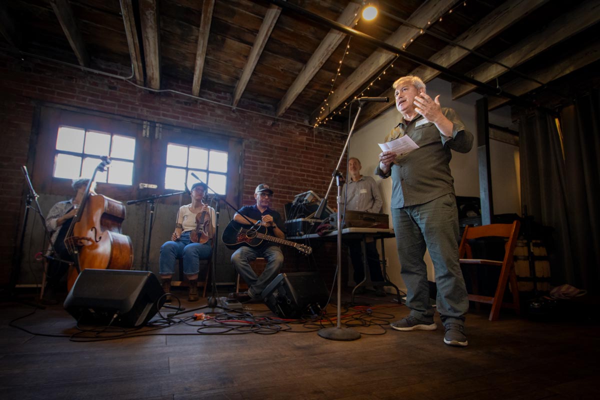 Man gives speech in a hayloft with a string band behind him.