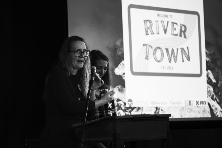 two speakers at a podium in front of a slide that has the River Town logo